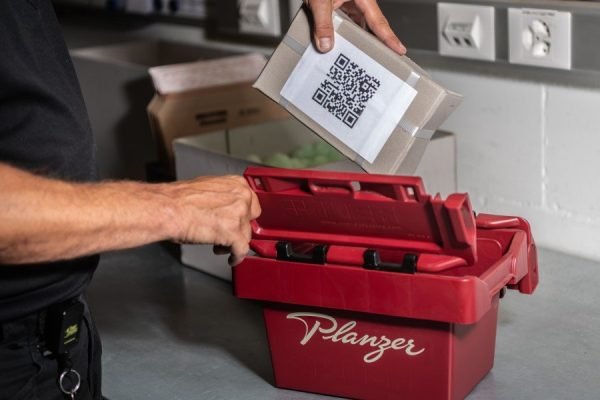 Paket mit QR-Code wird in rote Planzer-Sicherheitsbox gelegt