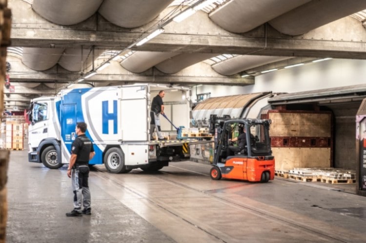 Helveticor-Fahrzeug bei der Beladung durch Mitarbeitende in einer Lagerhalle mit Gabelstapler
