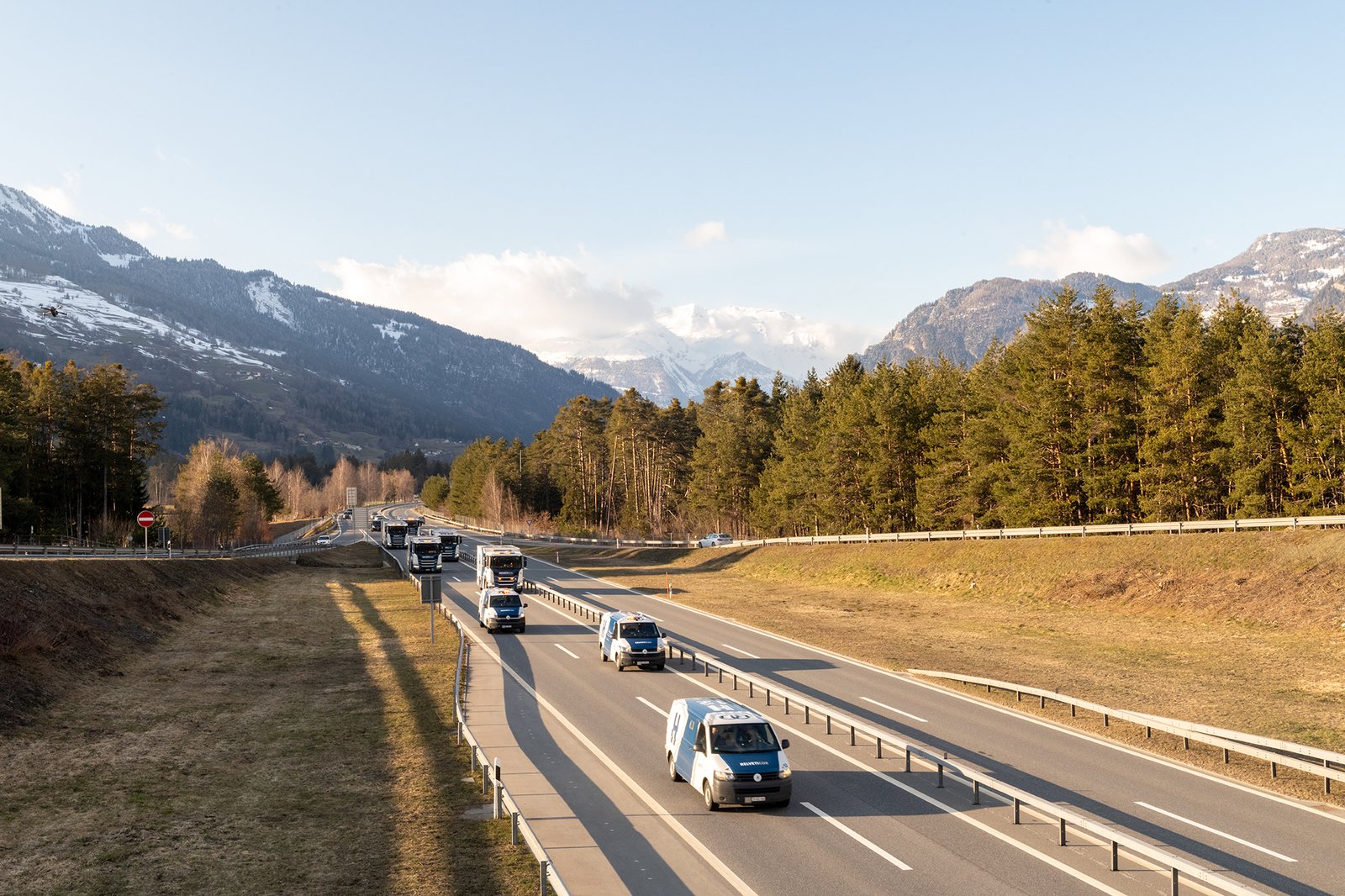 Mehrere Helveticor-Fahrzeuge in Kolonne auf einer Schweizer Autobahn mit Alpenpanorama