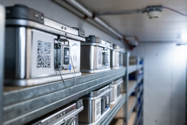 Lagerregale mit versiegelten Metallboxen zur Palladiumaufbewahrung, inklusive QR-Code und Überwachungskamera im Hintergrund