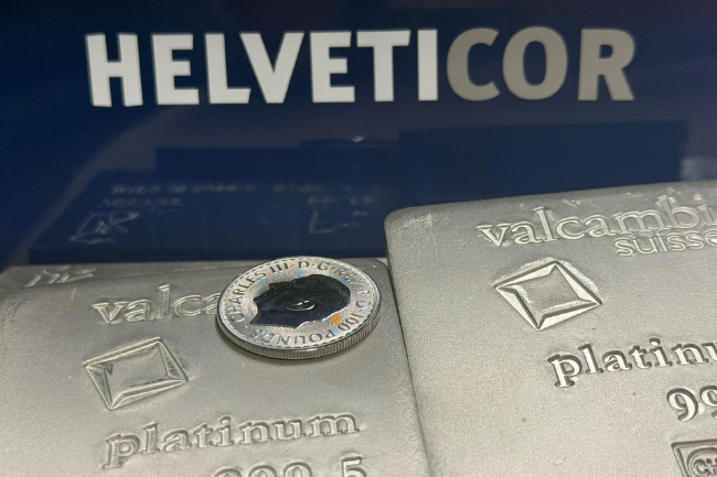 Zwei geprägte Platinbarren von Valcambi mit einer aufgelegten Münze, im Hintergrund das Helveticor-Logo